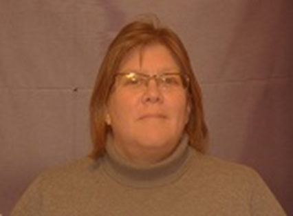 Portrait de Carolyn souriant à l’appareil photo et portant un col roulé beige.  Elle a les cheveux brun et porte des lunettes. 