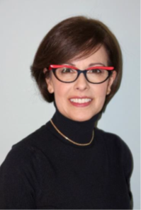 Woman with light skin and short dark hair smiling and wearing dark glasses and black turtleneck