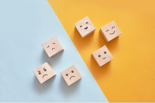 Une image contenant des blocs avec des visages aux sentiments variés et séparés en deux côtés : en colère, triste, fatigué, et content, joyeux, heureux.