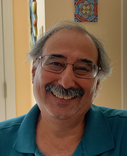 Picture of a smiling man with light skin brown skin, grey hair and moustache wearing a blue shirt and glasses.