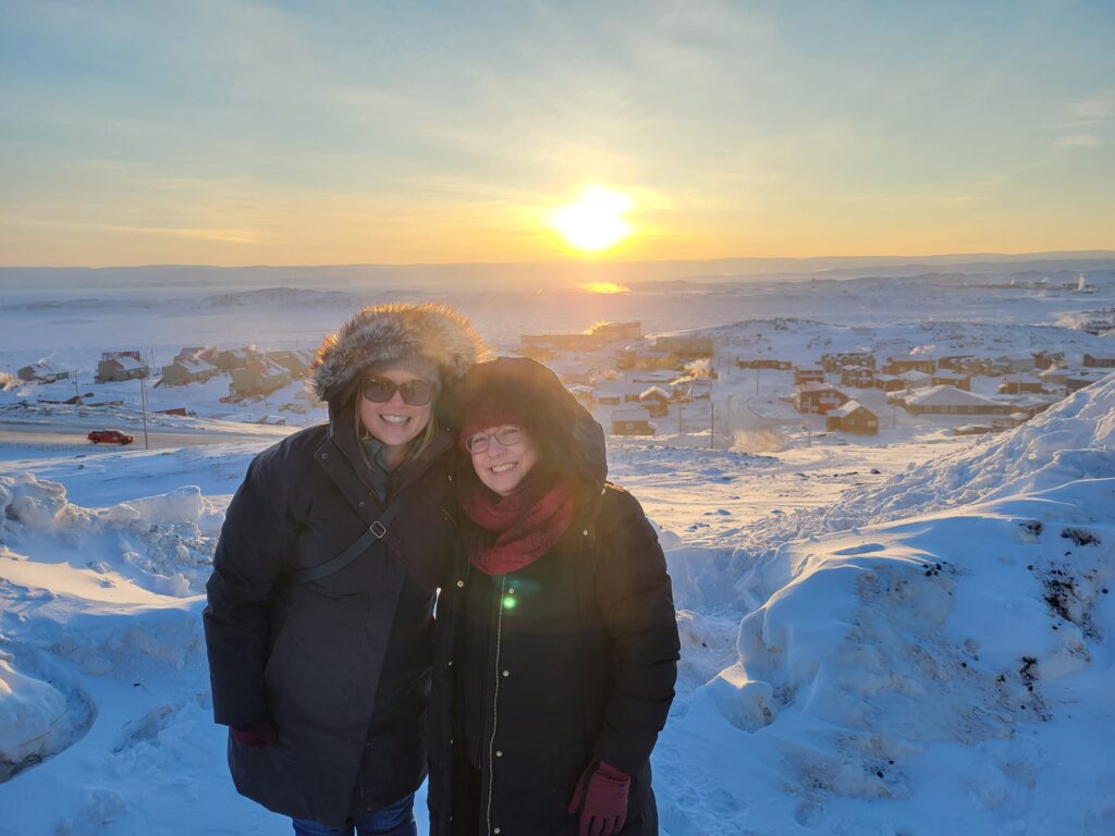 Photo de la directrice de la CNG, Camille, et de Martine, représentante du Québec et du Nunavut, à Iqaluit devant un coucher de soleil.