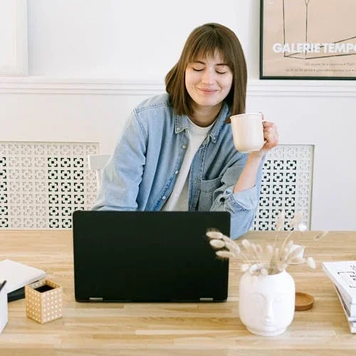 An image of a person working at a computer and drinking a coffee.