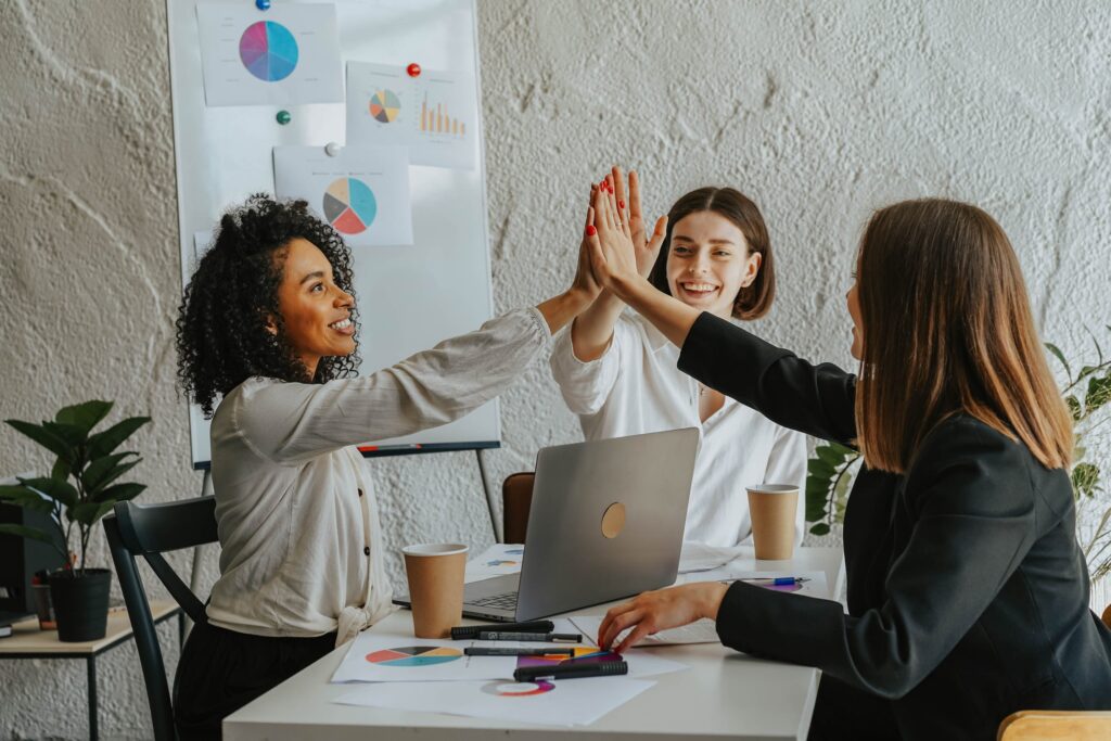 An image of three colleagues in a boardroom smiling and giving each other high-fives.