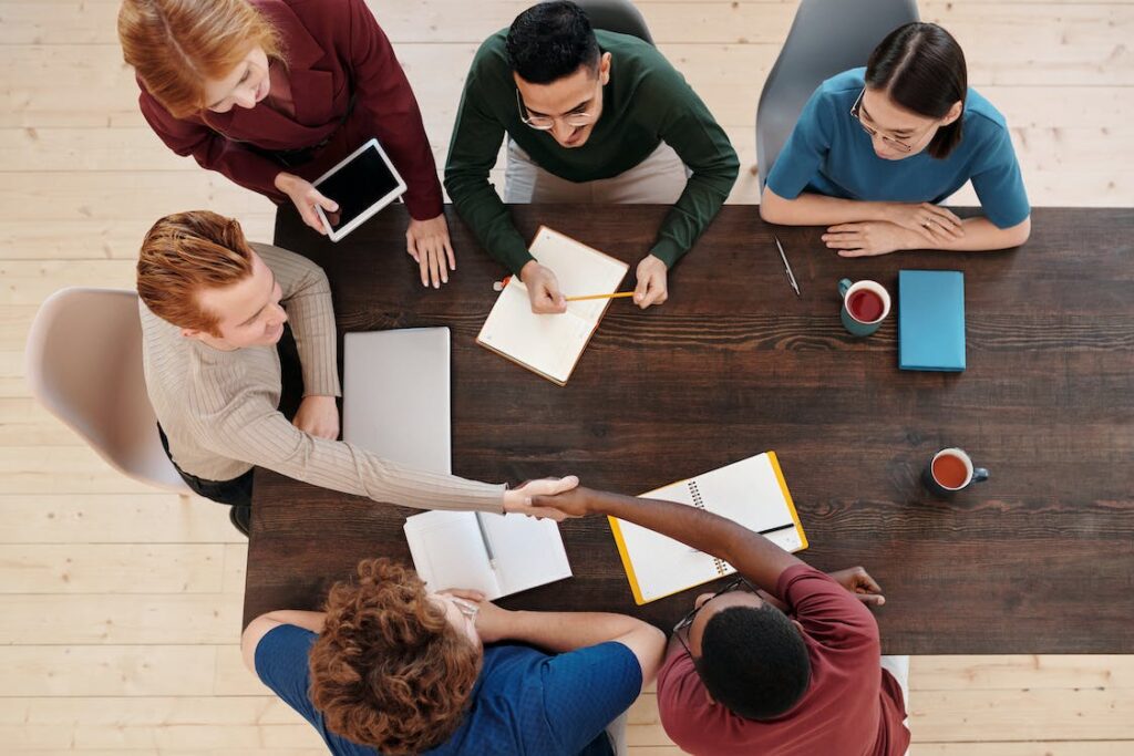 An image of six colleagues at a meeting table where two of them are shaking hands.