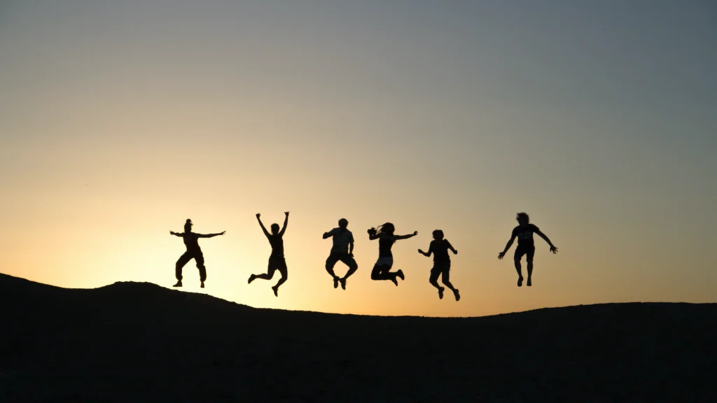 An image of a group of people jumping on a hill at sunset.