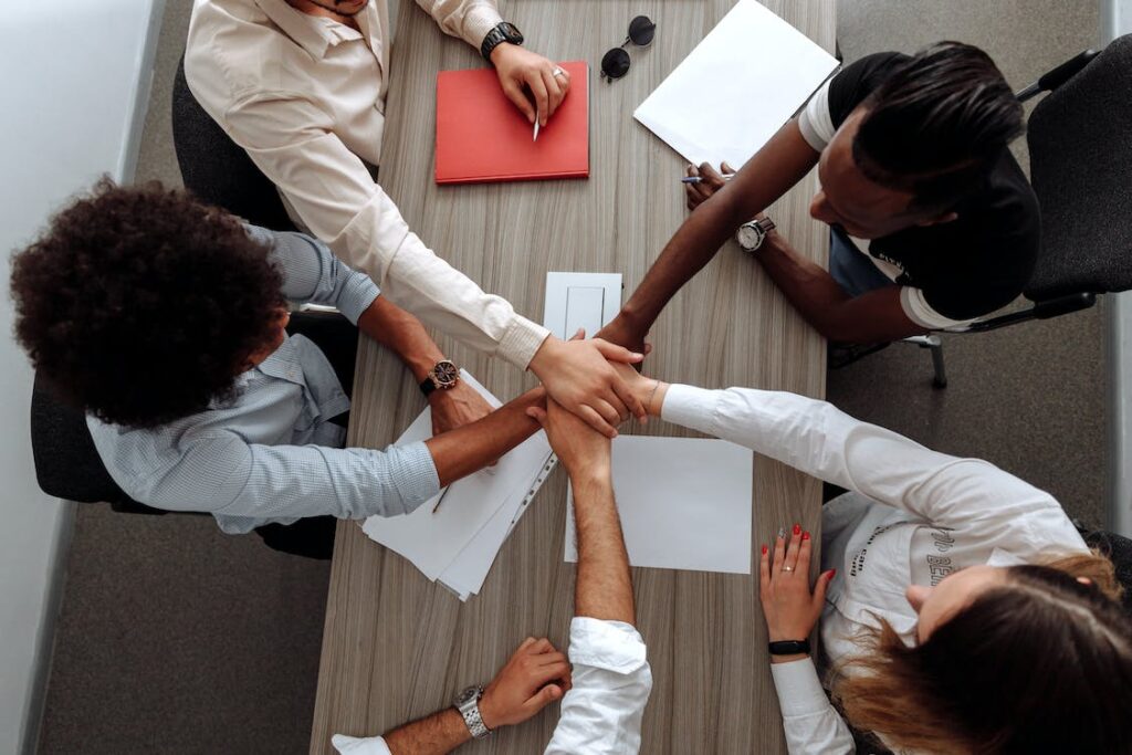 An image of five colleagues bringing their hands together in the middle of a table.