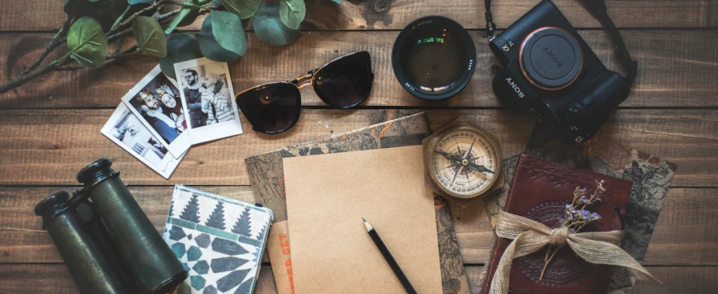 Une photo d'une paire de jumelles, de photos, d'une paire de lunettes, de carnets de notes et d'un appareil-photo étalés sur une table en bois.