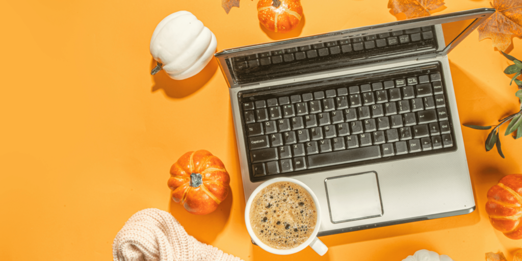 An image of a laptop against an orange background that is surrounded by pumpkins, leaves and a coffee cup.